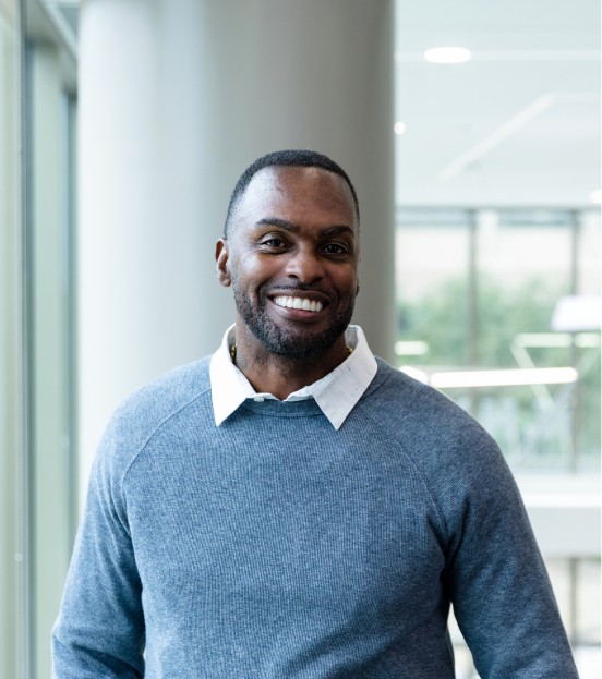 A portrait photo of a businessman in a white collard shirt and blue sweater smiling at the camera