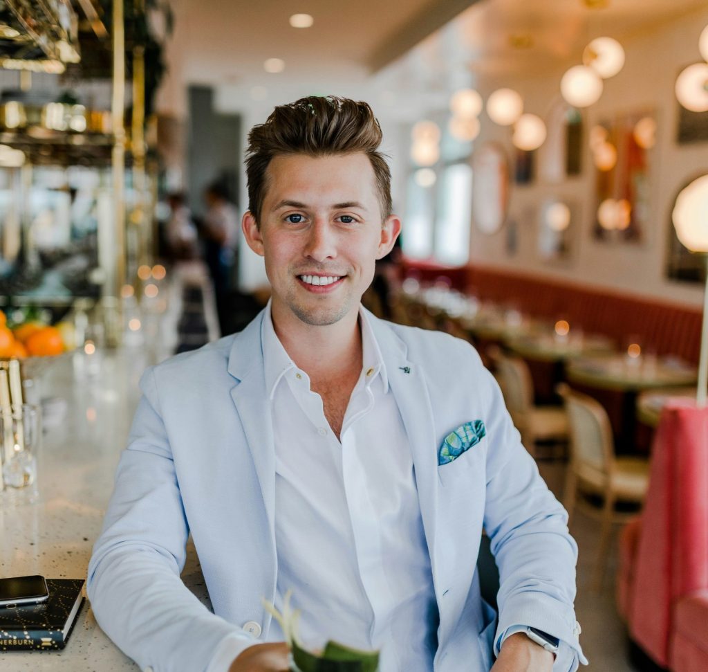A young professional in a white button down and light blue blazer leaning against the bar