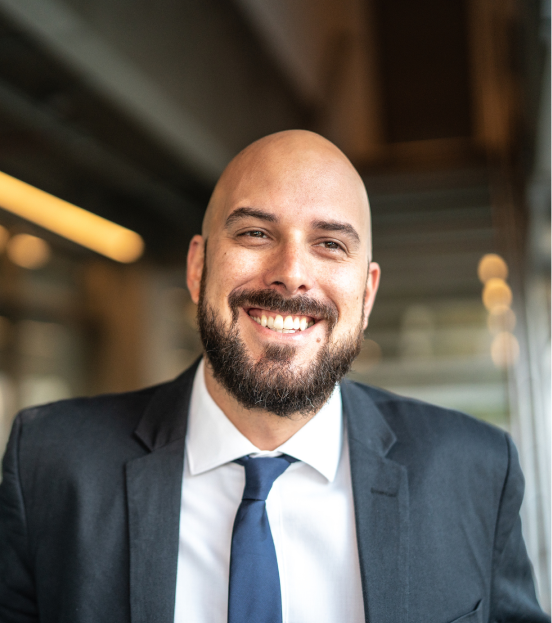 A portrait photo of a mature businessman in a grey suit jacket and navy blue tie smiling at the camera